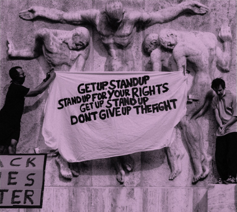 Two people holding a sign that reads "Get up. Stand up. Stand up for your rights. Get up. Stand up. Stand up for your rights."